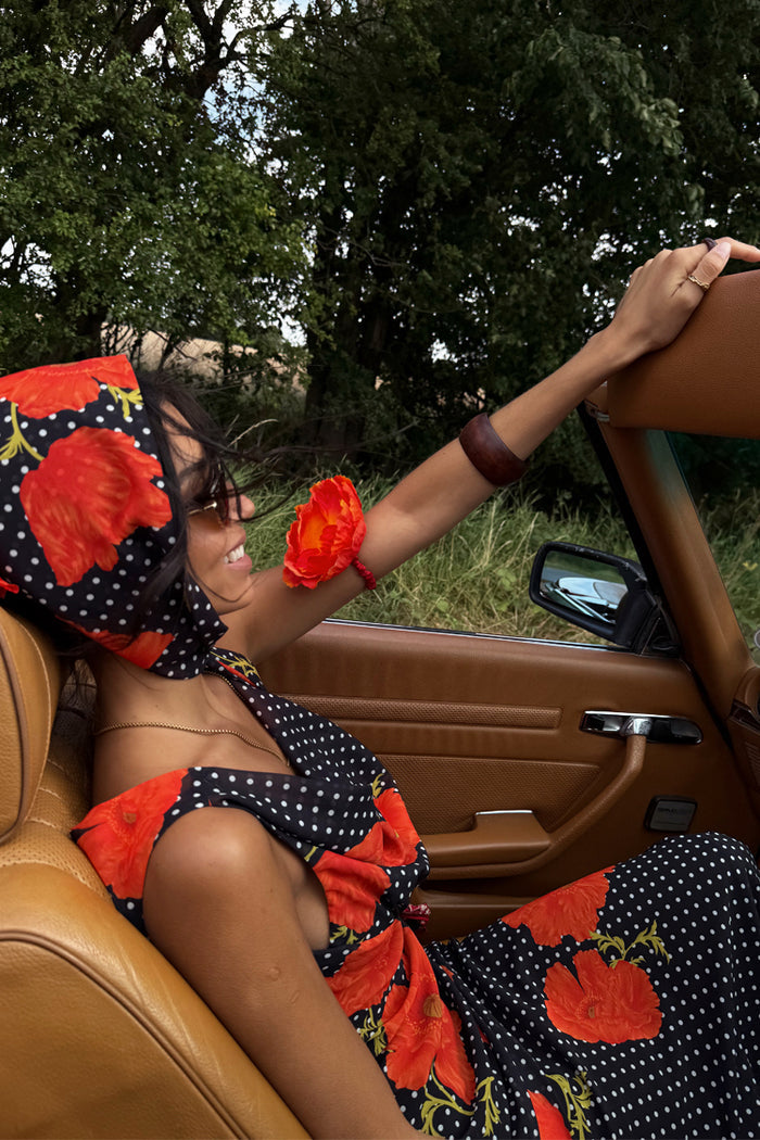 Black Poppy Sophie Dress with red poppy print and polka dots, worn with a matching headscarf in a vintage car.
