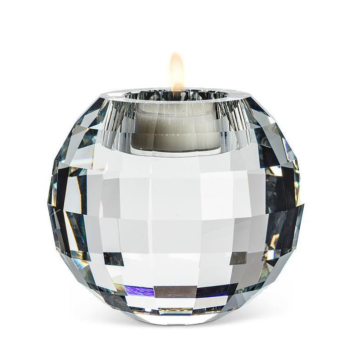 A faceted clear glass candle holder with a lit white tea light candle inside, set against a plain white background.