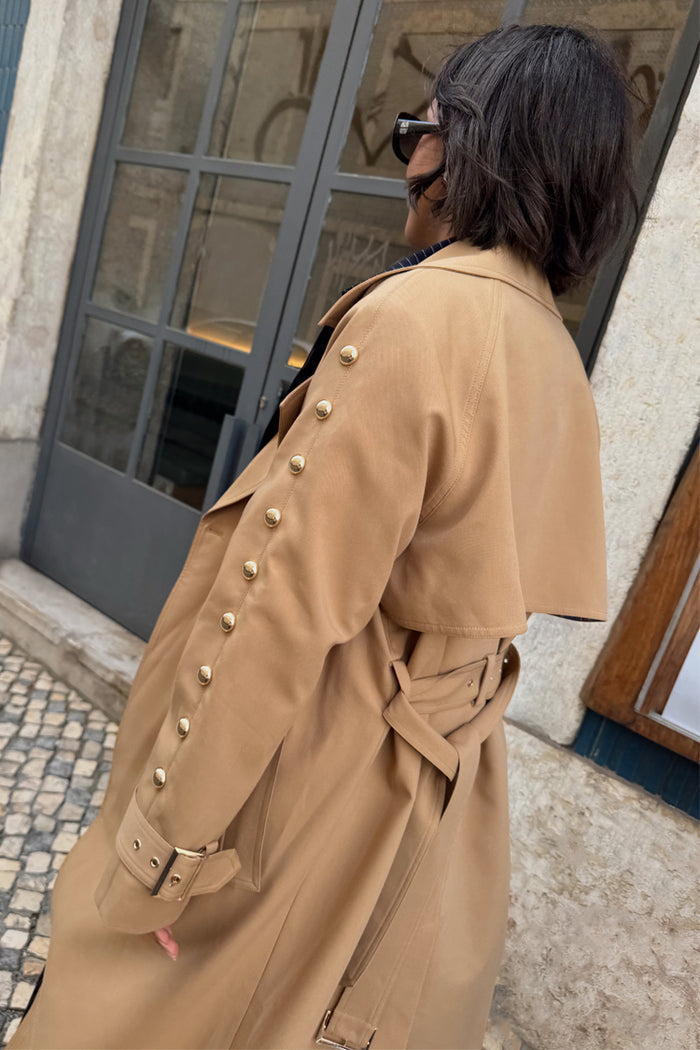 Tan Trench Coat with gold studs on the sleeves and a belted waist, designed in London for outdoor styling.