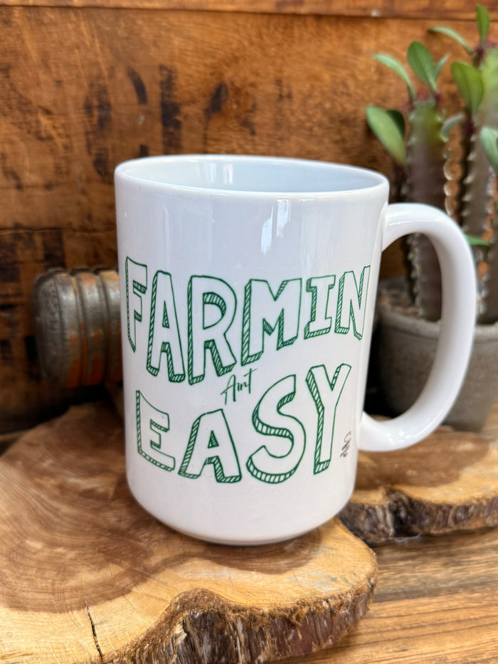 White ceramic mug with green 'FARMIN' AIN'T EASY' logo text on front and handle