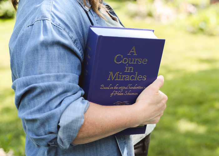 A person holding the large purple hardcover edition of A Course in Miracles Complete and Annotated Edition to show size and scale.