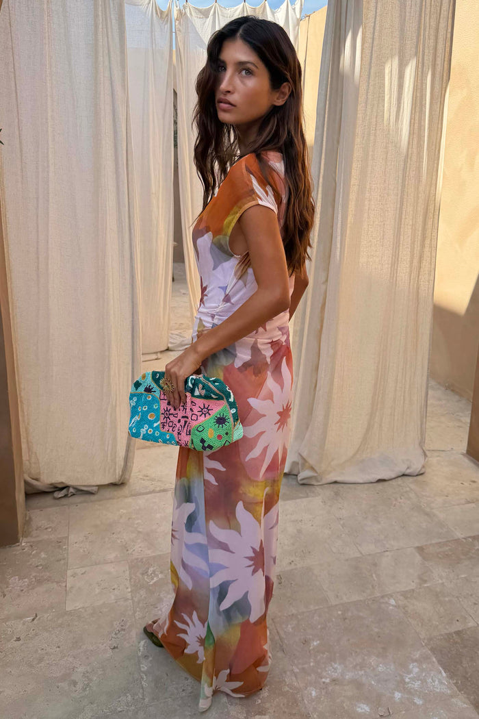 Soleil Luna Mesh Dress featuring an abstract sun print and a side-ruched detail, paired with a beaded clutch.
