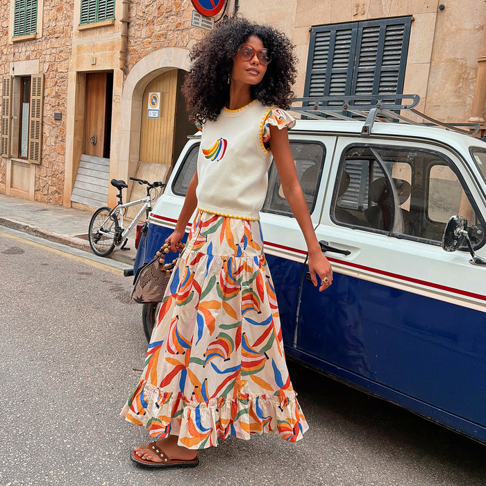 Banana Saige Skirt in a multicolour banana print with a tiered frill hem, styled on a model by a vintage car.
