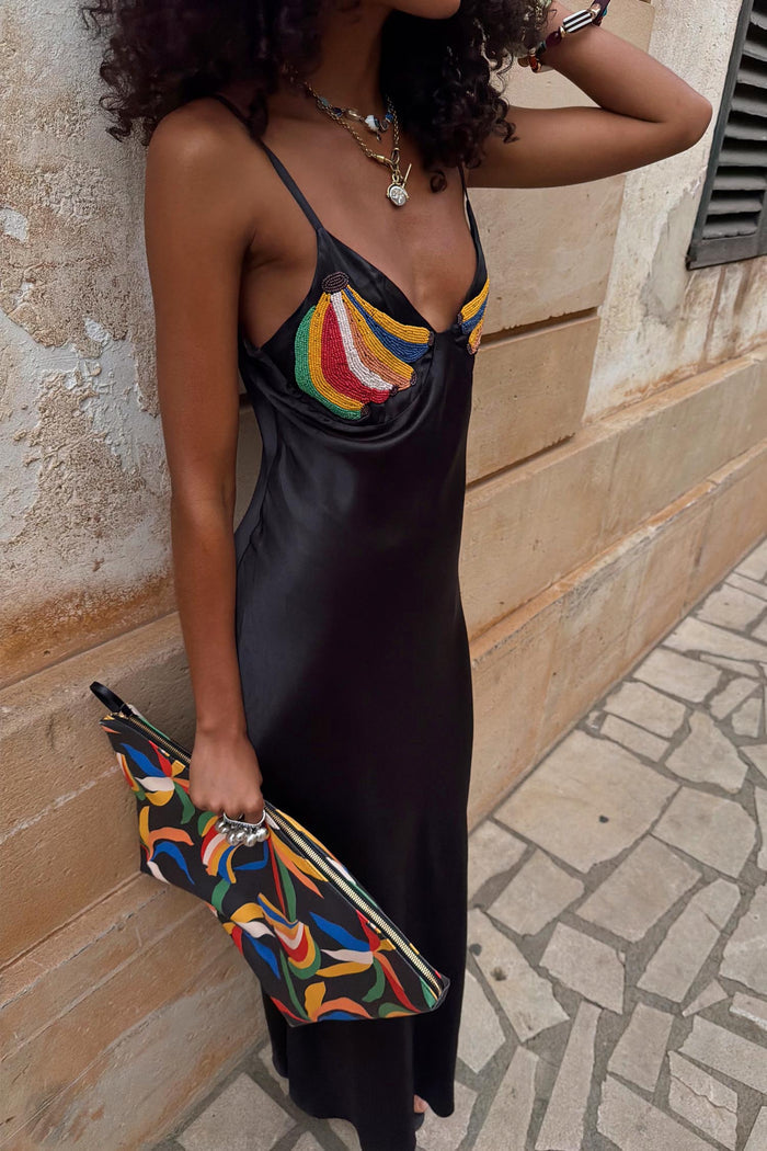 Black Banana Slip Dress featuring colourful beaded banana motifs on the bust, styled with a patterned clutch bag.
