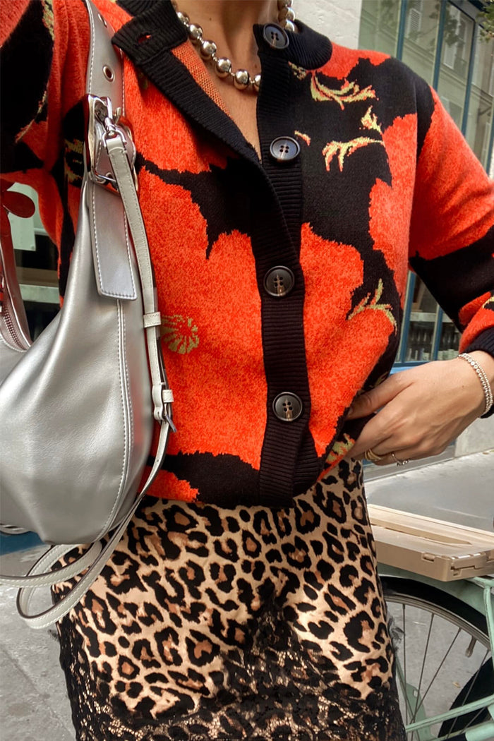 Black Poppy Cardigan with a bold poppy print and button-up front, styled with a leopard print skirt and silver bag.