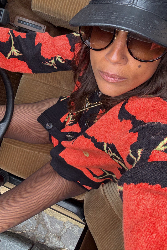 Black Poppy Cardigan with a bold red floral print, styled with fishnet tights and a cap in a vintage car.