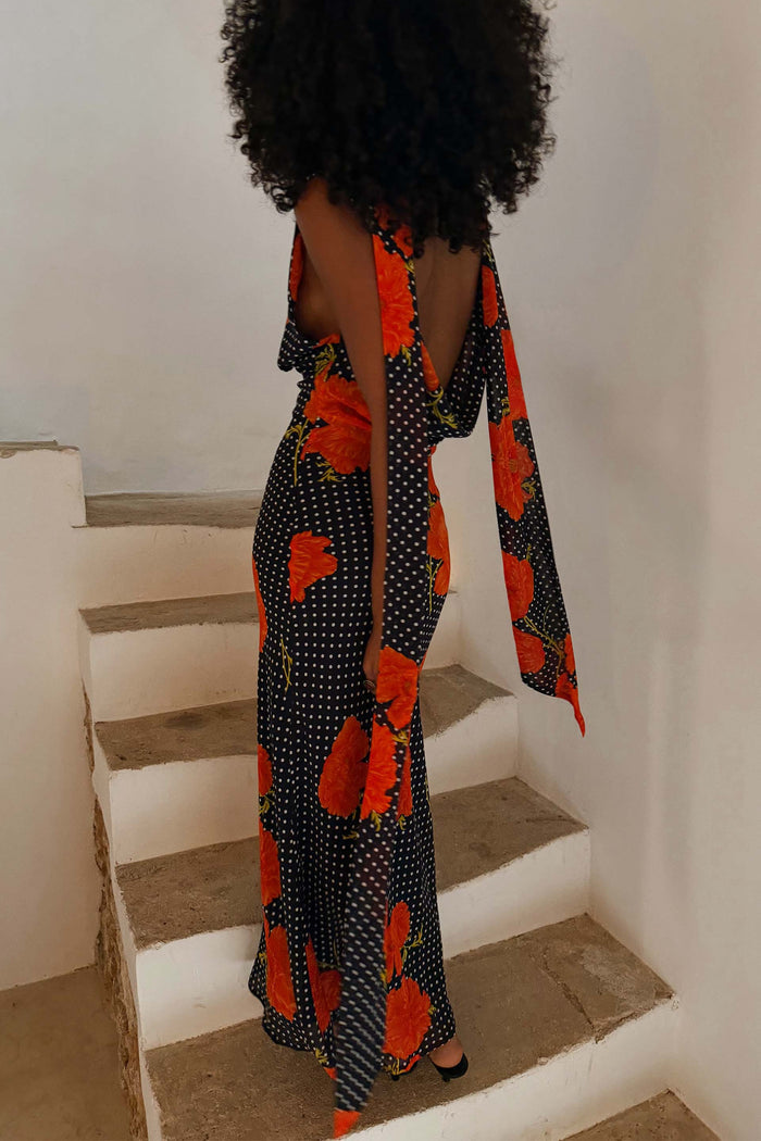 Black Poppy Sophie Dress featuring a poppy and polka dot print, low back and multi-wear scarf shown on stairs.