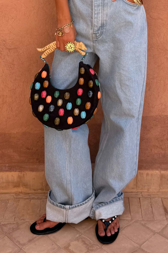Black Stone Beaded Bag featuring multicoloured stones and a sculpted wooden handle, held against light blue denim jeans.