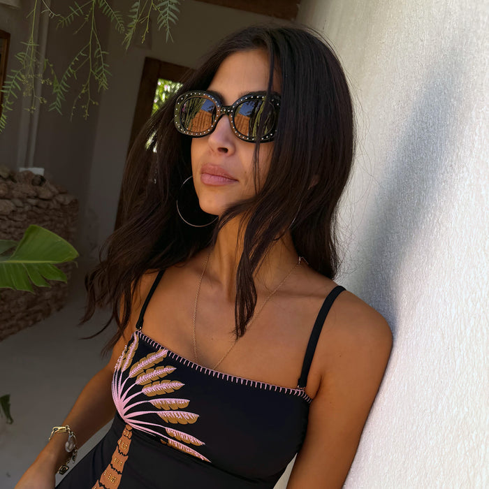 Black acetate sunglasses with silver studs and tinted lenses, worn with a palm tree print swimsuit.