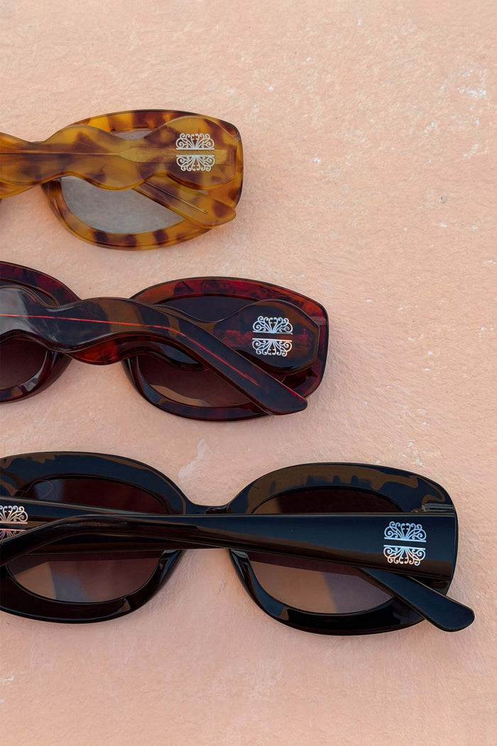 Black Studded Acetate Sunglasses with silver detailing, shown alongside tortoiseshell variations on a textured background.