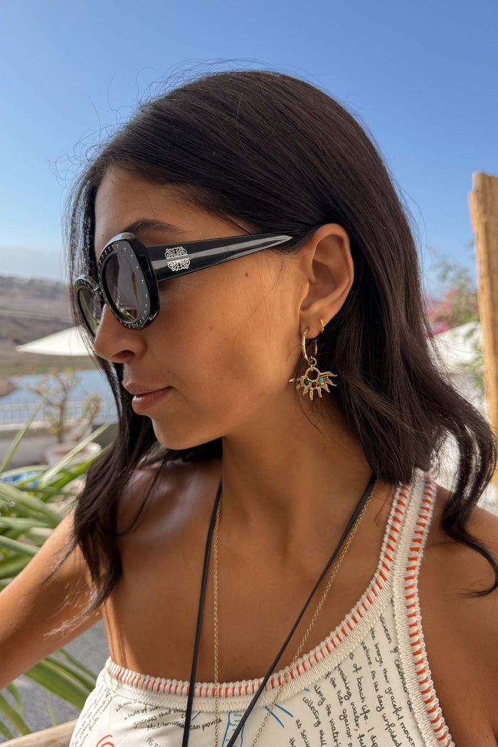 Black Studded Acetate Sunglasses with silver detailing and branding, worn by a model in an outdoor vacation setting.