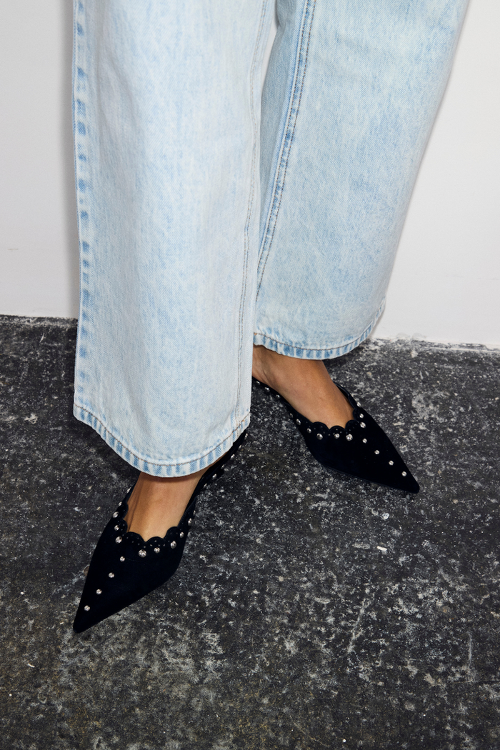 Black Suede Mules featuring scallop edging and silver studs, paired with light-wash blue jeans.