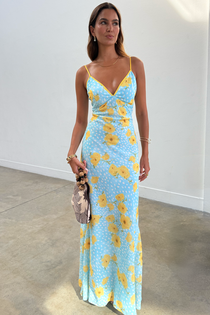 Blue Fawn Poppy Elsie slip dress with yellow poppy and fawn spot prints, styled with a beaded bag.