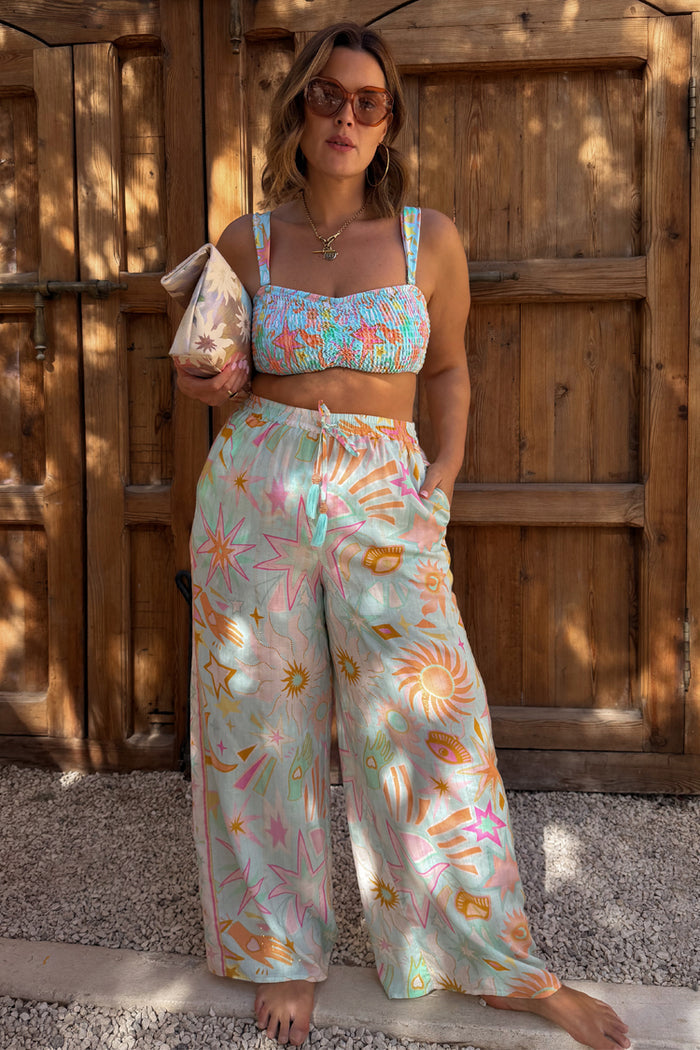Blue Dreamer Shirred Bandeau Top with a sun and palm print, styled with matching trousers for a vacation look.