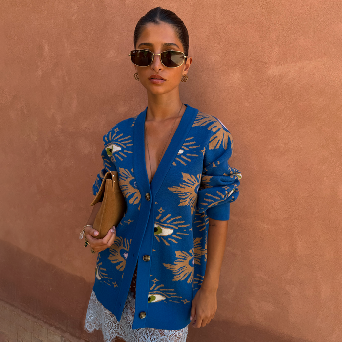 Relaxed fit Blue Eye Cardigan with iconic eye motifs, layered over a lace slip dress and tan clutch.