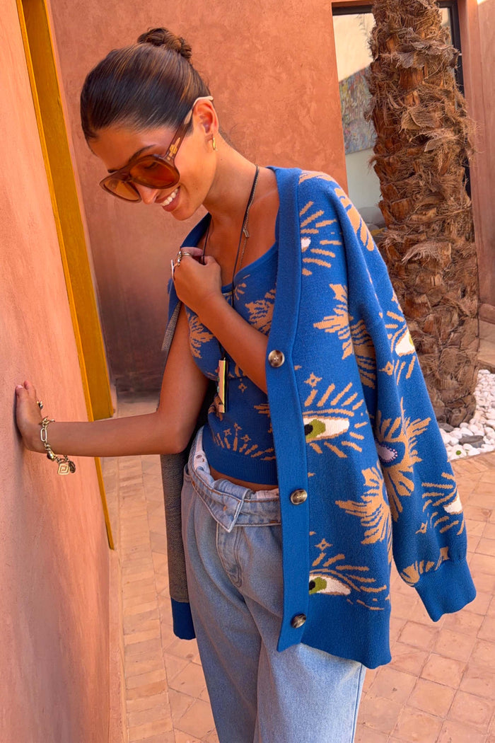 Iconic Blue Eye Cardigan featuring eye motifs, layered over a matching knit top and light blue denim jeans.