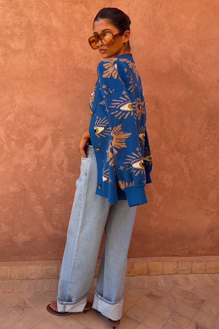 Blue Eye Cardigan featuring knitted eye motifs, styled with light wash denim jeans and sunglasses.