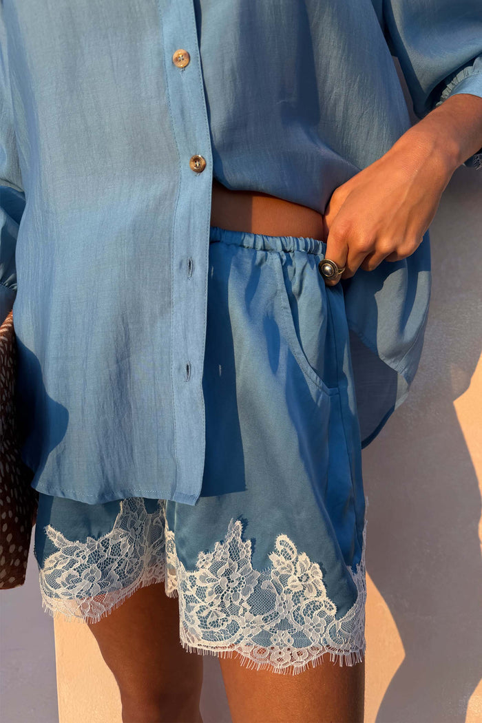 Blue Lace Maeva Shorts in a washed blue tone with satin fabric, white lace trim and an elasticated waistband.
