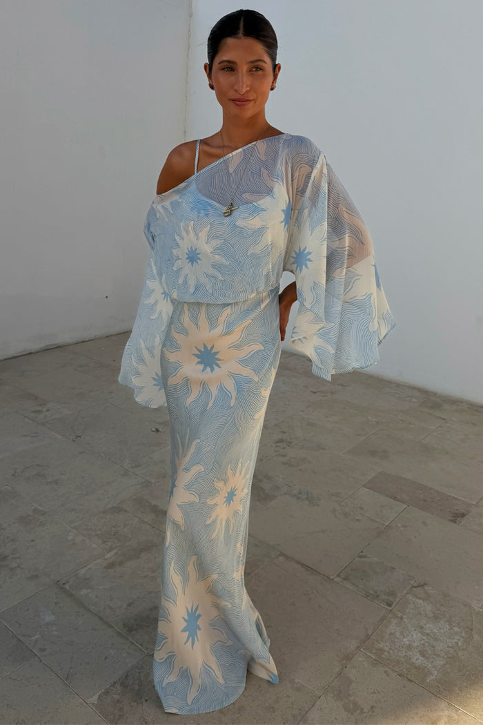 Blue Soleil Anais Dress with a Mediterranean sun print, draped sheer off-shoulder top, and sleek bias-cut skirt.