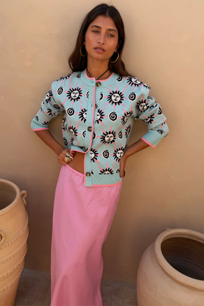 Blue Sun Hollie Cardigan in a baby blue soft touch knit with a pink sun print, paired with a pink satin skirt.