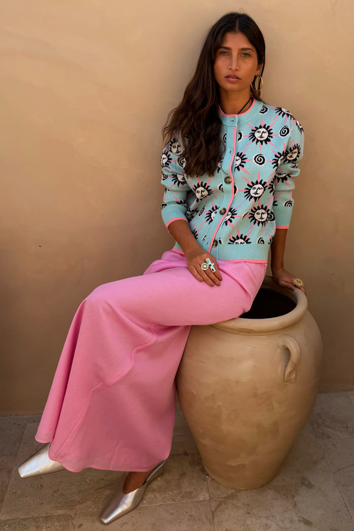 Blue Sun Hollie Cardigan in baby blue with a pink sun print, styled with a long pink skirt and silver shoes.
