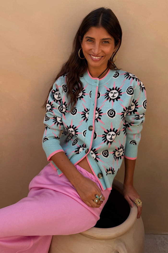 NFD Blue Sun Hollie Cardigan in baby blue soft-touch knit with a pink sun print, worn by a model.