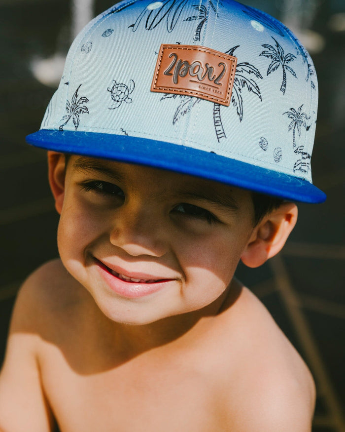 Deux par Deux boys' blue beach print flat-brim cap – close-up on a smiling boy