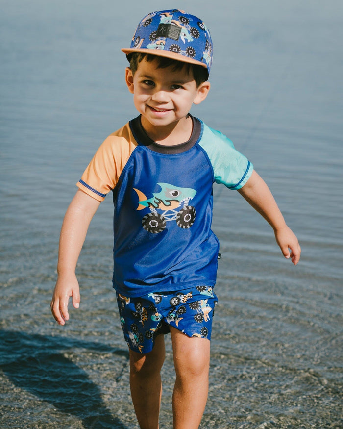 Deux par Deux boys' blue monster truck print flat-brim cap – worn by a boy at the beach
