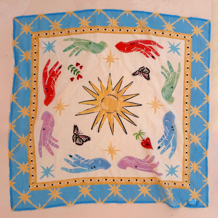 Celestial Bandana featuring a blue star border and hand-painted sun, palm, and mystical hand motifs on a cream base.