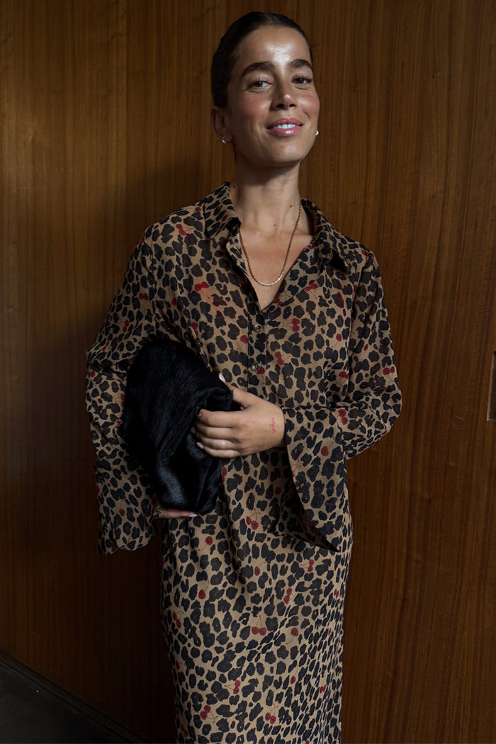 Cherry Leopard Mia Dress featuring a shirt-style top and red cherry detailing, styled with a black clutch.