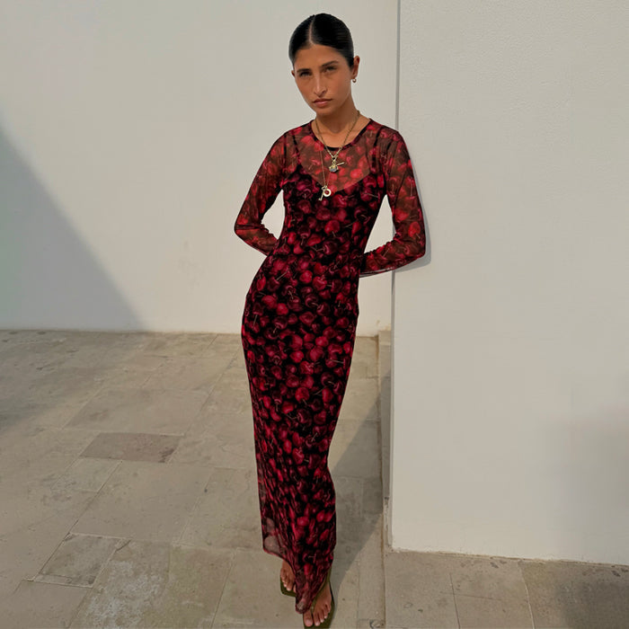 Red digital cherry print Mesh Soho Dress with long sleeves, designed in London and worn by a model against a wall.