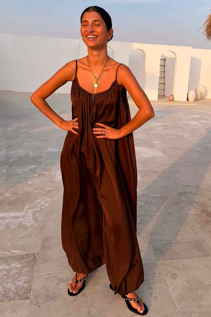 Chocolate Balloon Jumpsuit featuring a draped silhouette, gathered neckline and slim straps on a smiling model.