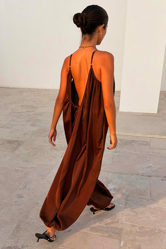 Chocolate Balloon Jumpsuit with a deep V back and draped silhouette, shown on a model walking outdoors.