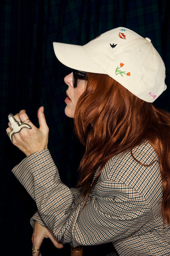 Cream Choose Love Cap with colourful embroidered icons, worn by a red-haired woman in a checkered blazer.