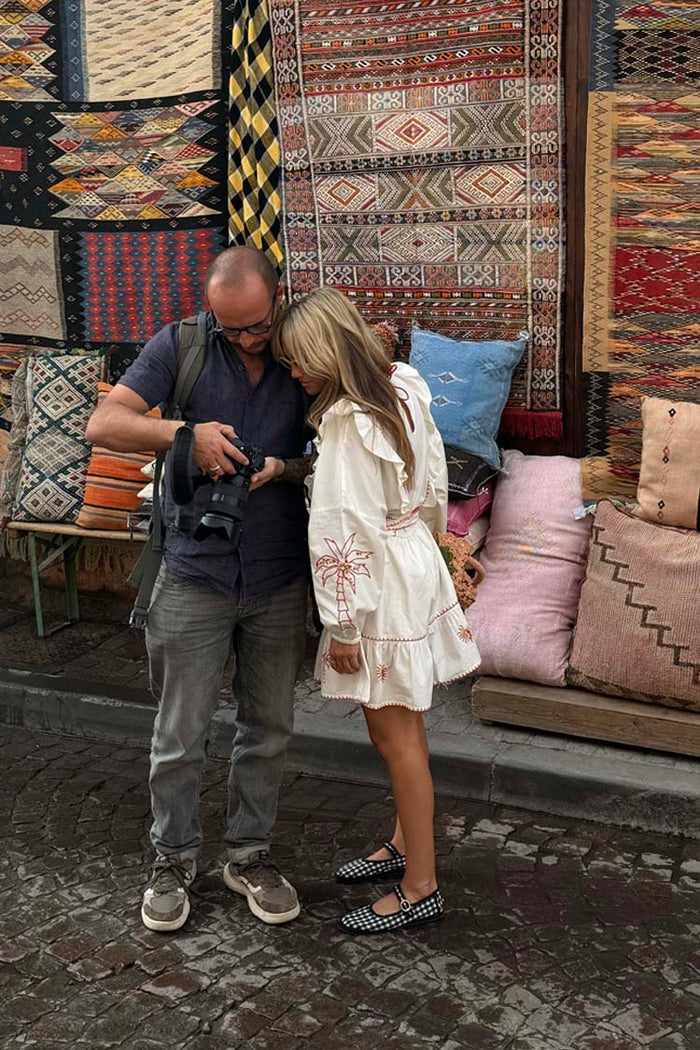 Cream and Red Pollenca Mini Dress with palm tree embroidery and ruffles, worn by a model in a vibrant market setting.