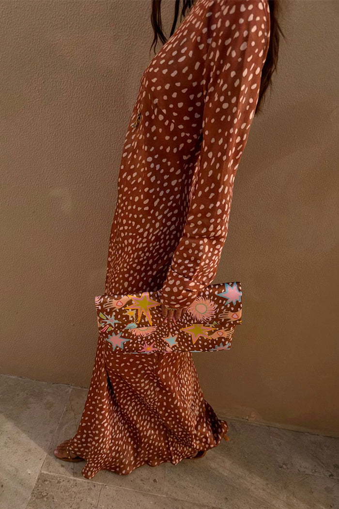 Fawn Soho Dress in brown and cream spotted satin, shown from the side with a star print clutch.
