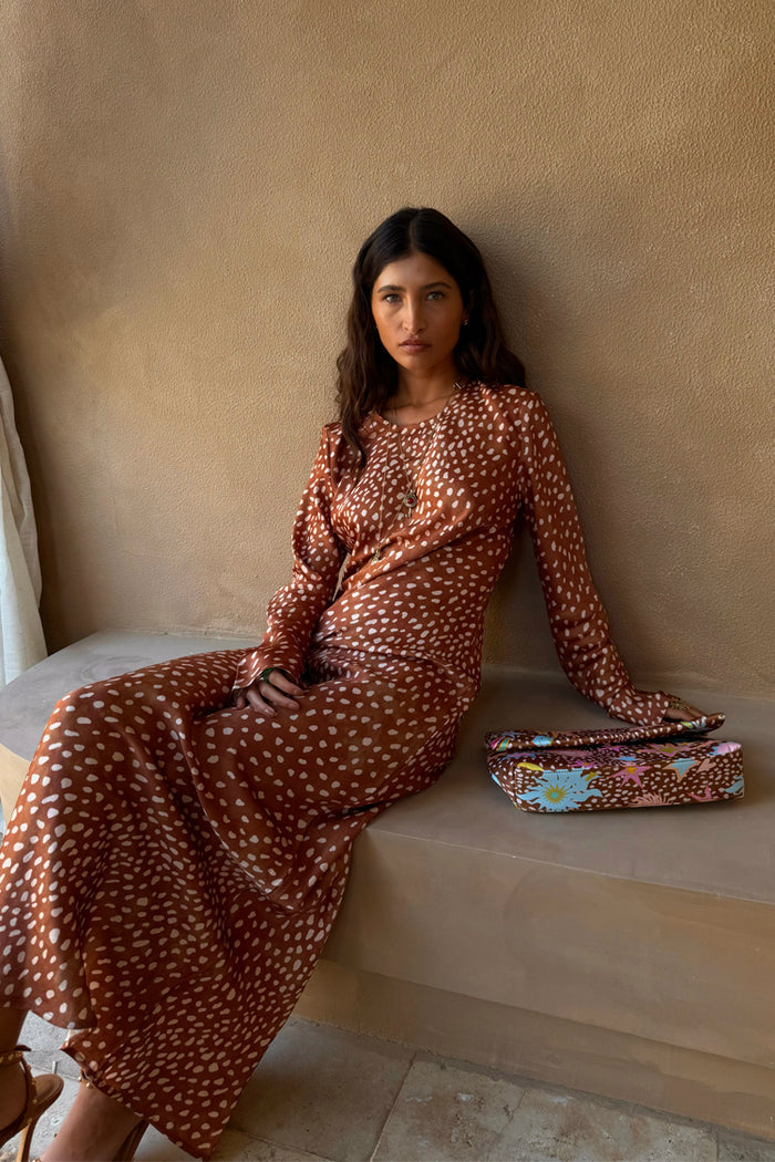 Fawn Soho Dress in brown satin-esque deer print with long sleeves, shown on a seated model with a printed clutch.