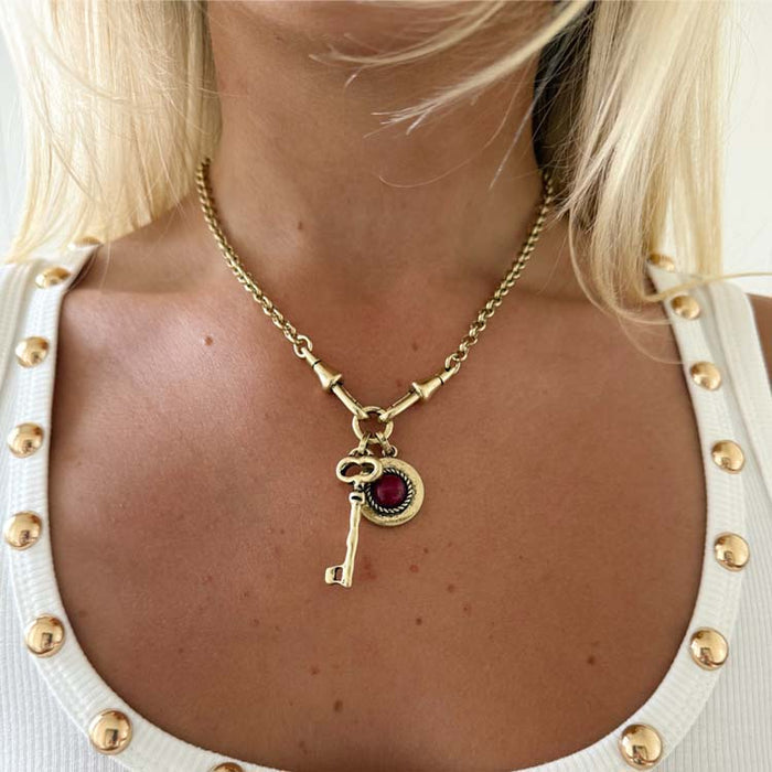 Deloris Key Necklace with red gemstone and key pendants on a polished brass link chain.