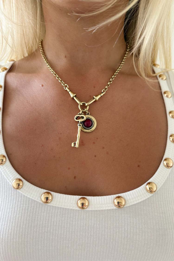 Iconic Deloris Key Necklace with a gold brass key pendant and red gemstone charm, styled on a model.