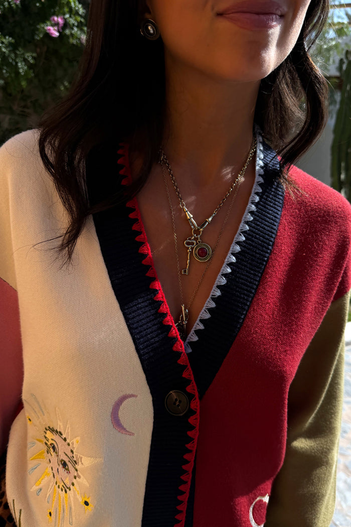 Deloris Key Necklace in brass with a red gemstone pendant, layered over a sun-embroidered cardigan.