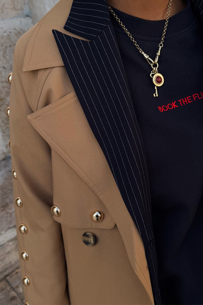 Deloris Key Necklace with a red gemstone on a brass link chain, layered over a navy pinstripe blazer.
