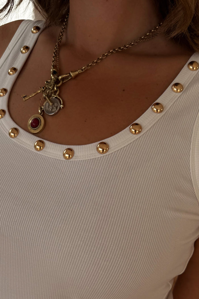 Deloris Key Necklace with iconic key and red gemstone charms on a polished brass chain, styled for layering over a vest.