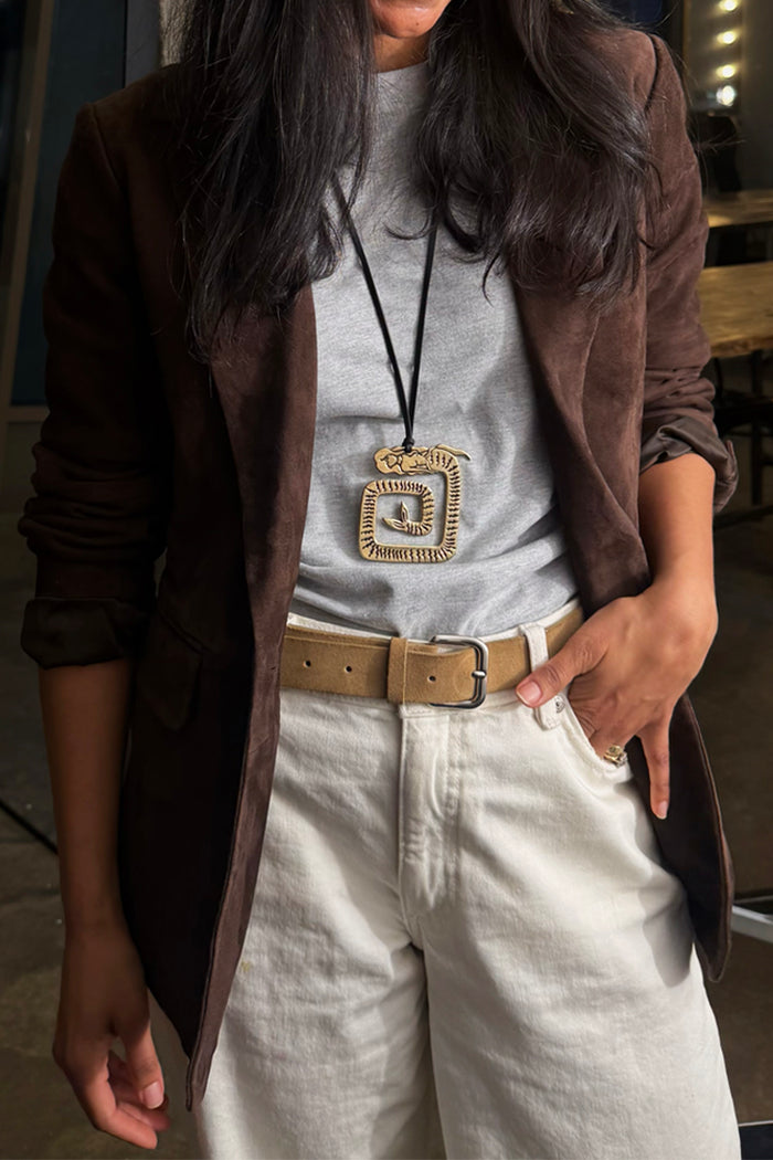 Deloris Mermaid Necklace featuring an engraved brass pendant on a black leather cord, styled over a brown blazer.