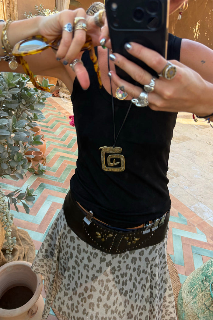 Deloris Mermaid Necklace with an engraved brass pendant on an adjustable leather cord, worn with a leopard skirt.