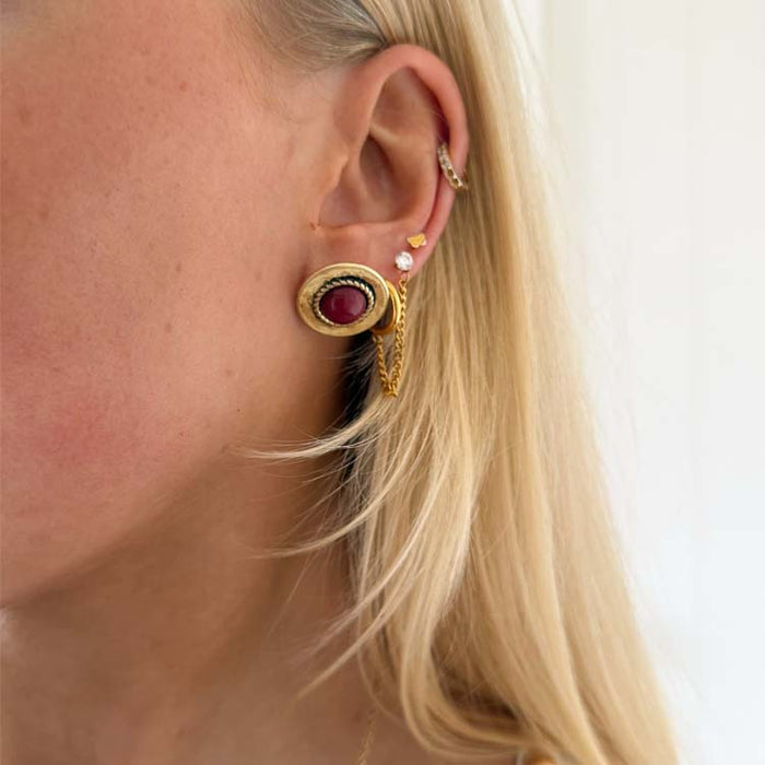 Deloris Red Circle Earrings featuring a red semi-precious stone and textured brushed brass on a model's ear.