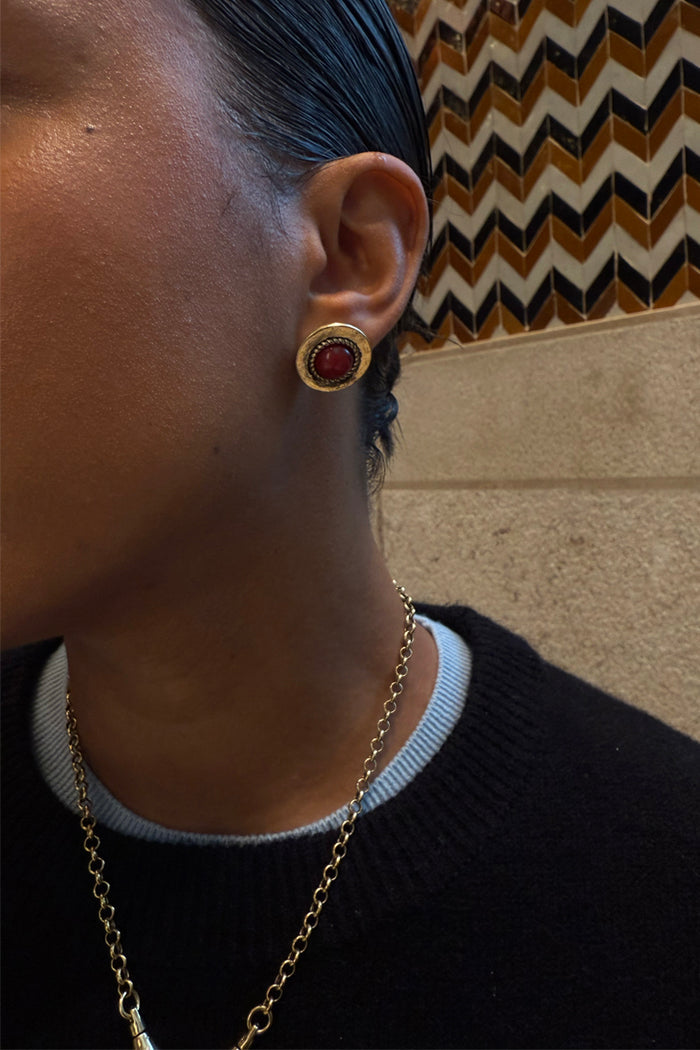 Deloris Red Circle Earrings in textured brushed brass with a semi-precious red stone, shown on a model.