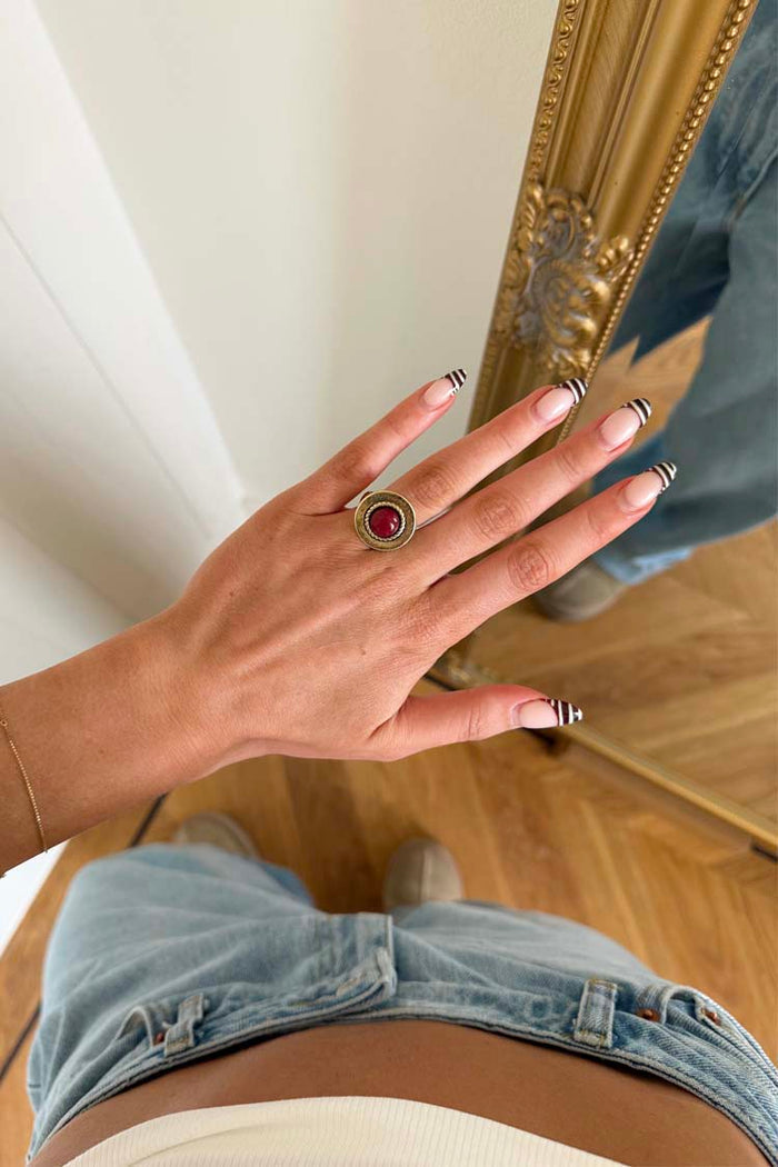 Textured brass Deloris Red Circle Ring with a red semi-precious stone, worn on a hand over light-wash jeans.