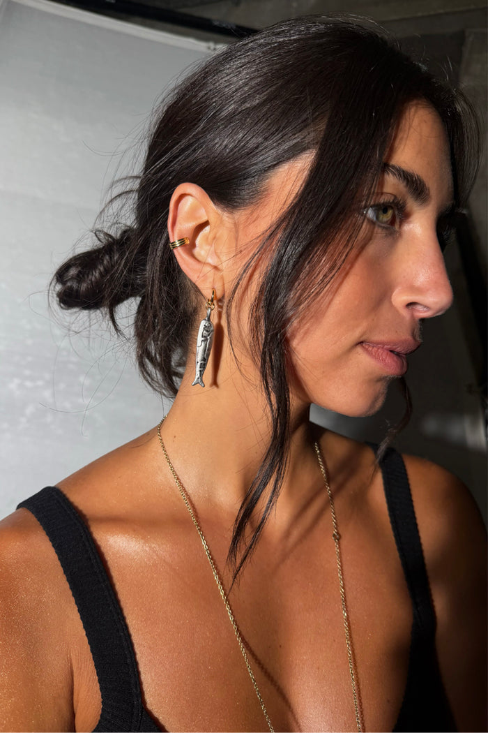 Deloris Sardine Earrings featuring mixed-metal fish pendants on gold hoops, worn by a model in a black tank top.