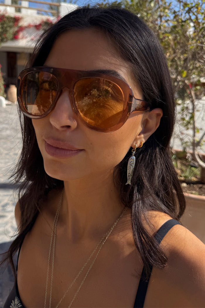 Deloris Sardine Earrings in mixed-metal brass with an intricate fish pendant, styled on a model for a vacation look.