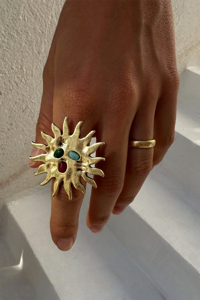 Deloris Sun Ring in brass with a large sun motif and colourful semi-precious stones, worn on a hand.